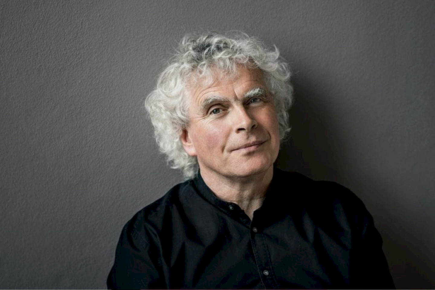 Dirigent Simon Rattle vor grauem Hintergrund